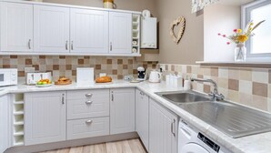Een moderne keuken met witte kasten, een roestvrijstalen spoelbak, een magnetron, een broodrooster en een koffiezetapparaat.