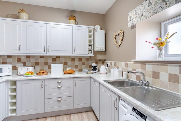 A modern kitchen with white cabinets, a stainless steel sink, a microwave, a toaster, and a coffee maker.