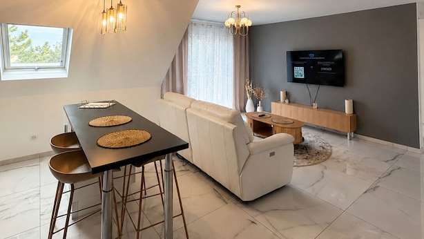 A modern living room with a dining area, a sofa, a TV, and a ceiling light fixture.