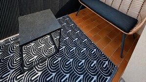 A rooftop terrace with a patterned rug, a bench, and a wall with vertical lines.