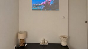 A room with a mounted TV displaying a movie, a black console table with decorative items, a lamp, and a door.