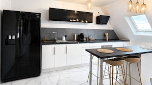 A modern kitchen with a black refrigerator, white cabinets, a black countertop, and a skylight.
