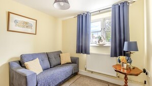 Una habitación con un sofá gris, una mesita con una lámpara y una ventana con cortinas.