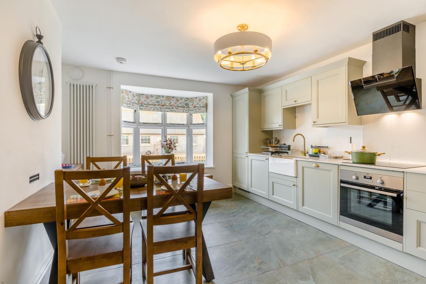 A kitchen with a dining table and chairs, a window, cabinets, a stove, and a wall-mounted clock.