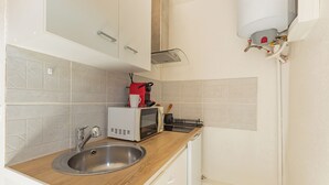 Cozinha com pia de aço inoxidável, micro-ondas e chaleira vermelha.