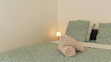 Ein Bett mit einem blumigen Überwurf, einem zusammengerollten Handtuch und zwei Kissen im gleichen Muster.