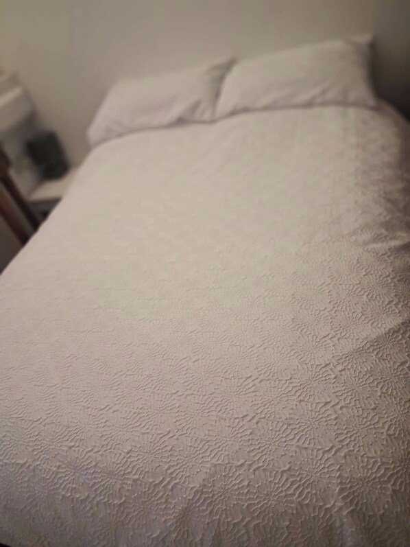 A bed with a textured white cover and a pillow. - Porthleven Studio, Sleeps 3, Patio & Beach Access (Helston)