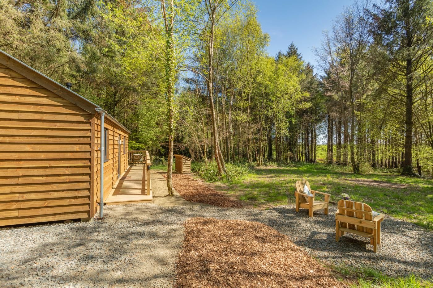 A wooden cabin with a deck, surrounded by a forest.