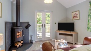 Ein Wohnzimmer mit Kaminofen, Fernseher und Essbereich mit Tisch und Stühlen.