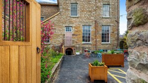 A stone building with a wooden door, a paved courtyard, and outdoor seating. - 1 Bed in Presteigne (oc-t38200) (Presteigne)