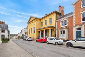 Eine Straße mit geparkten Autos und Gebäuden, darunter ein gelbes Gebäude mit Säulen.
