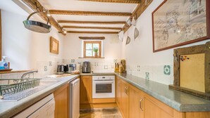Een compacte keuken met houten kastjes, een Bosch vaatwasser, een koffieapparaat en een raam voor natuurlijk licht.
