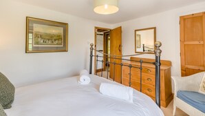 Een slaapkamer met een bed, een houten dressoir, een spiegel en een schilderij aan de muur.