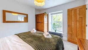 Een slaapkamer met een bed, een houten garderobe, een spiegel, een raam en een hanglamp.