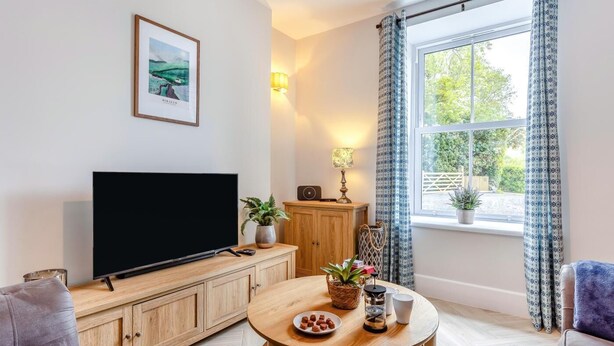 Een woonkamer met een televisie, een houten kast, een ronde tafel met hapjes en een raam met gordijnen.