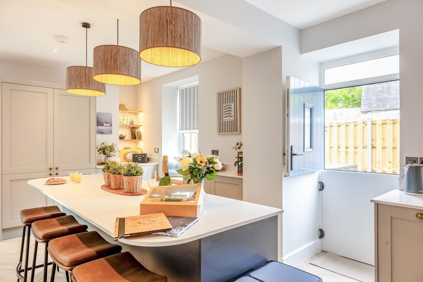 A modern kitchen with a central island, pendant lights, and a view of the outdoors.