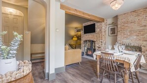 A dining area with a brick fireplace, wooden furniture, and a television mounted on the wall. - 2 Bed in Sydling St. Nicholas (oc-a39901) (Sydling Saint Nicholas)