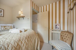 A bedroom with a bed, a chair, a radiator, a door, and a wall-mounted lamp.