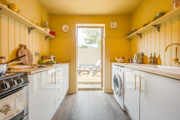 A compact kitchen with white cabinets, a stove, a washing machine, and a dining area visible through the door.
