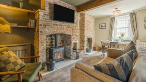 A cozy living room with a fireplace, a television mounted above it, and a dining area with a table and chairs. - 2 Bed in Sydling St. Nicholas (oc-a39901) (Sydling Saint Nicholas)