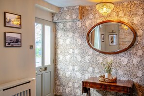 Ein Zimmer mit strukturiertem Wandpapier, einem runden Spiegel, einer Holzkommode und zwei gerahmten Bildern an der Wand.