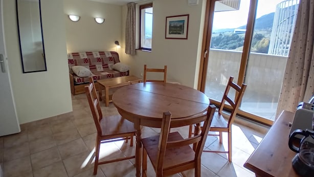 A dining area with a round wooden table and chairs, a sofa with a patterned cover, and a view through a sliding glass door. - Apartment for 4 People in Val Cenis (Val-Cenis)
