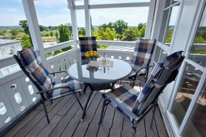 A covered outdoor seating area with a round table and chairs, a bottle of champagne, and a vase of yellow flowers. - Familienurlaub in Sellin mit Balkon (Sellin)
