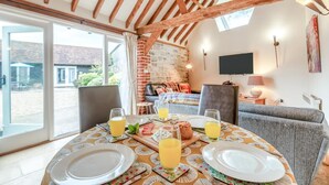 Un'area pranzo con un tavolo apparecchiato per due persone, un divano e una TV montata a parete.