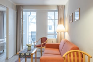 A hotel room with a sofa, a chair, a table with a vase, and a lamp. - Gemutliche Ferienwohnung im Seepark Sellin mit Balkon (Sellin)