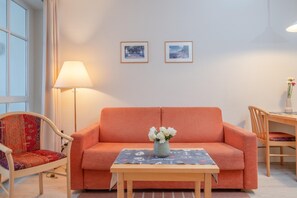 Ein Zimmer mit einer Couch, einem Tisch mit Blumenvase, einer Lampe und zwei gerahmten Bildern an der Wand.