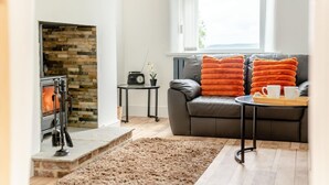 A living room with a fireplace, a sofa with orange cushions, a coffee table with a tray, and a small table with a radio and plant. - 2 Bed in Consett (oc-b42654) (Consett)
