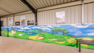 A covered outdoor area with a mural of a golf course, a sign for 'GoodDrive,' and several other signs advertising local businesses.
