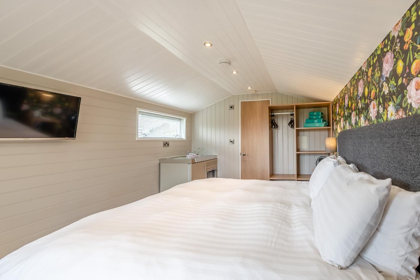 A bedroom with a bed, a television, a window, a wardrobe, and a bathroom.