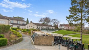 A golf course with a clubhouse, a parking area with golf carts, and residential buildings in the background. - 1 Bed in Lancashire (oc-w37869) (Bentham)