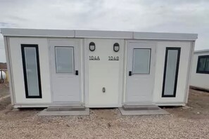 A portable building with two doors labeled 104A and 104B, each with a small window. - Private Duplex with Twin and Full Bunk Bed, Kitchenette and Private Bath (Pecos)