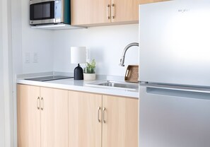 A modern kitchen with light wood cabinets, a stainless steel refrigerator, a microwave, a sink, and a small potted plant. - Private Duplex with Twin and Full Bunk Bed, Kitchenette and Private Bath (Pecos)