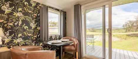 A room with a dining table, two chairs, a window, and a view of a grassy landscape.