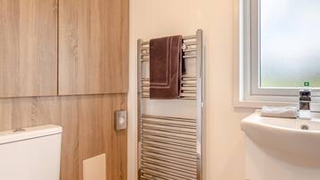 A bathroom with a white toilet, wooden cabinets, a towel rack, and a window.