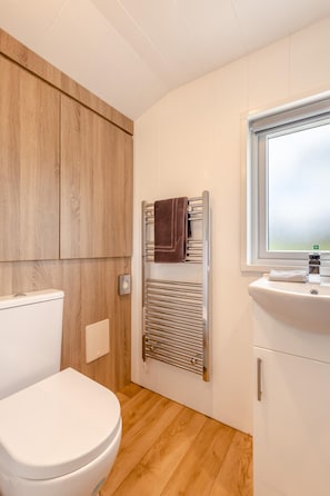 A bathroom with a white toilet, wooden cabinets, a towel rack, and a window.