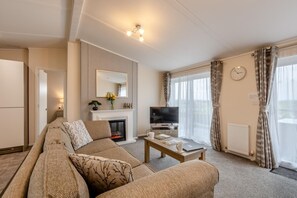A living room with a sofa, a television, a fireplace, and a dining area. - 2 Bed in Bentham (oc-d37872) (Bentham)
