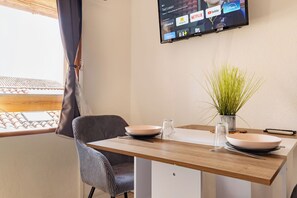 A dining area with a wooden table, two chairs, a vase with green plants, and a television mounted on the wall displaying various streaming services. - Downtown, Studio Apartment with 4 air conditioning units, Wi-Fi, Canal+, and a washing machine (Bédarieux)