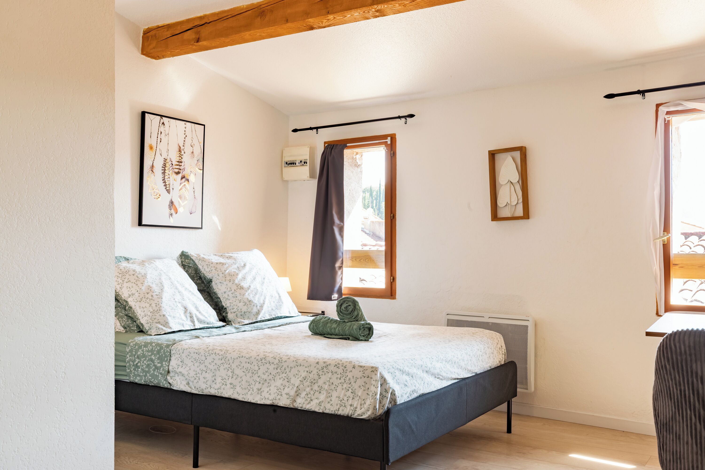 Un dormitorio con cama, un radiador, una ventana con cortinas y cuadros colgados en la pared.