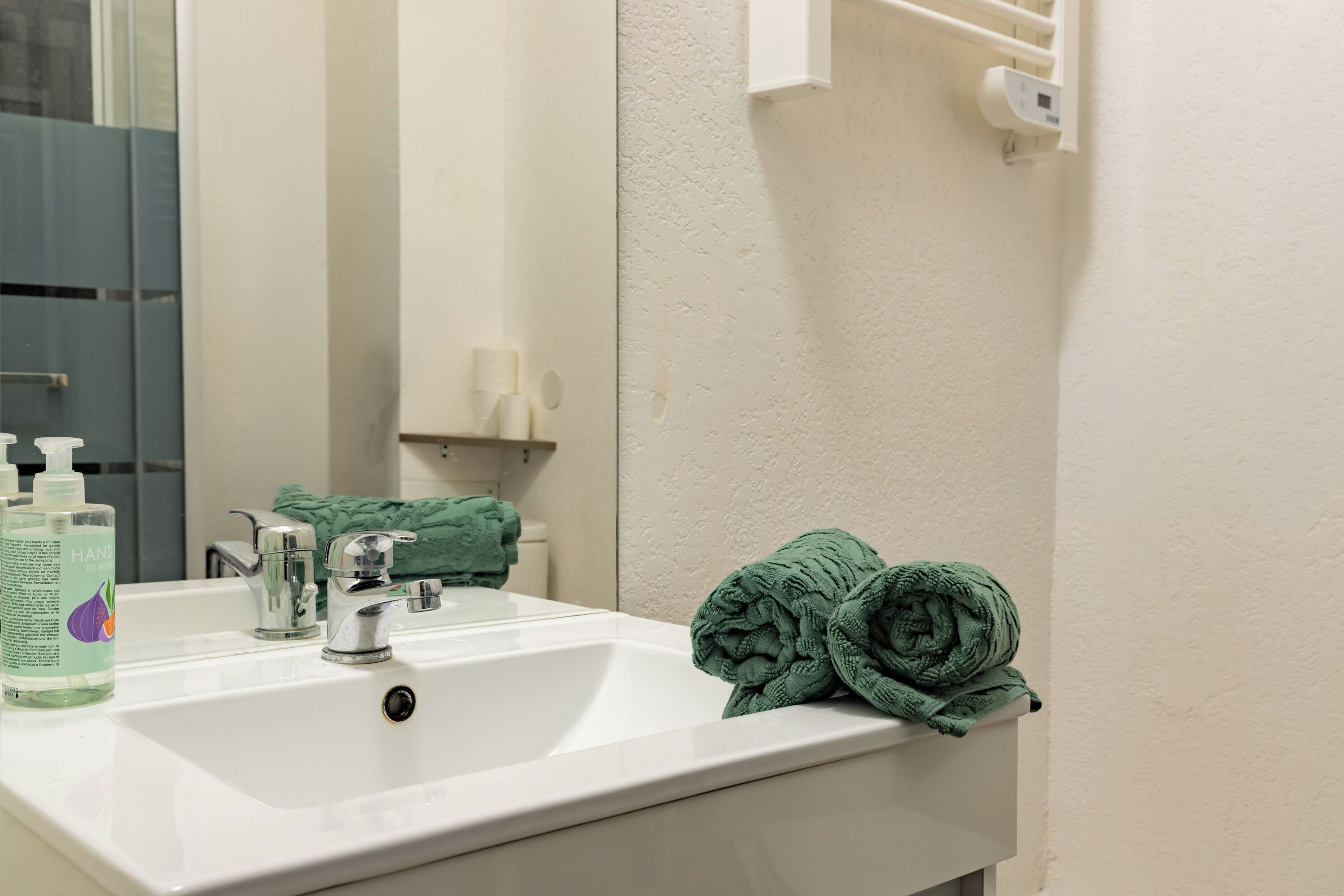 Een wastafel met spiegel, een groene handdoek en een fles handzeep.