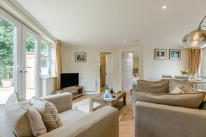 Ein modernes Wohnzimmer mit Flachbildfernseher, Sofas, einem Couchtisch und einem Essbereich mit Tisch und Stühlen.