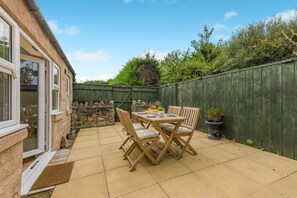 A patio with a table and chairs, a stone wall, and a wooden fence. - 2 Bed in Seahouses (oc-s42665) (Seahouses)