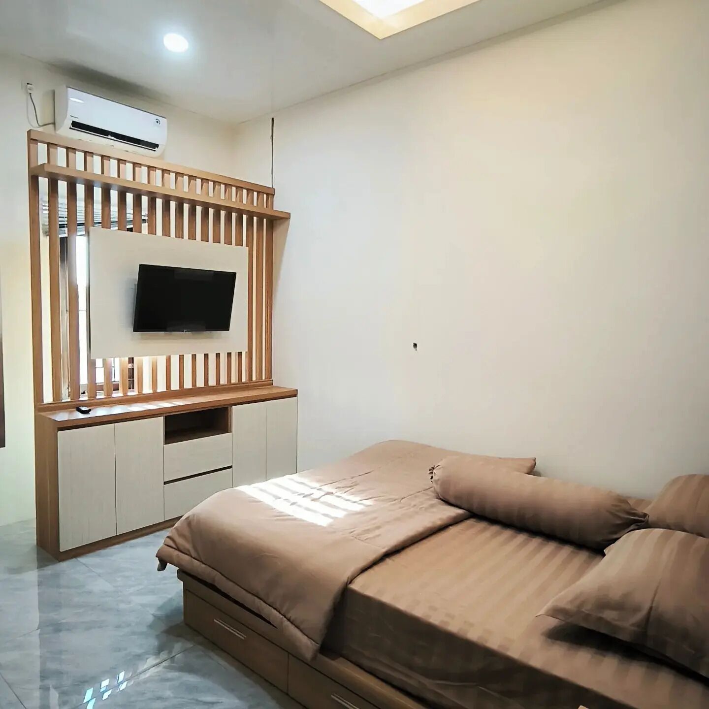Quarto com cama, TV fixada em um painel de madeira e ventoinha no teto.
