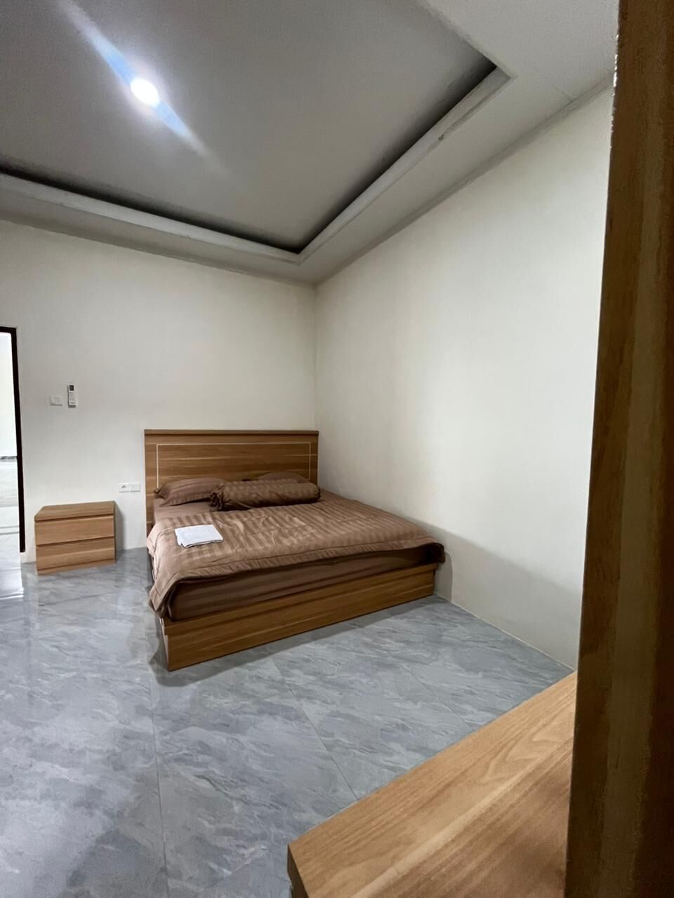 A bedroom with a bed, a nightstand, a wooden bench, and a ceiling light.