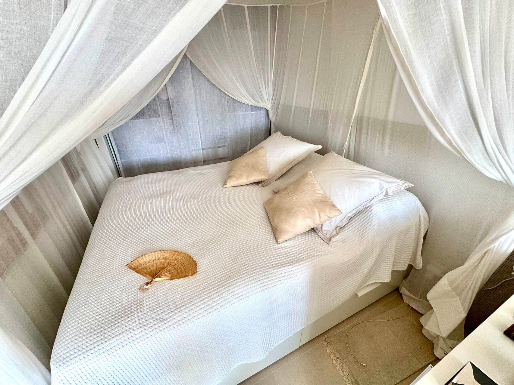 A bed with a canopy, pillows, and a woven basket.