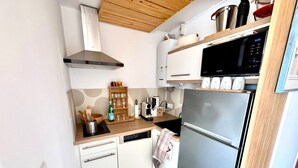 A compact kitchen with a stainless steel refrigerator, a microwave, and a wooden ceiling. - L’écrin Bleu – Sea View Apartment for 4 Guests (Le Cap d'Agde)
