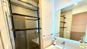 A bathroom with a glass shower enclosure, a white sink, and a mirror above it. - L’écrin Bleu – Sea View Apartment for 4 Guests (Le Cap d'Agde)